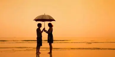 Two people standing on the beach under an umbrella.