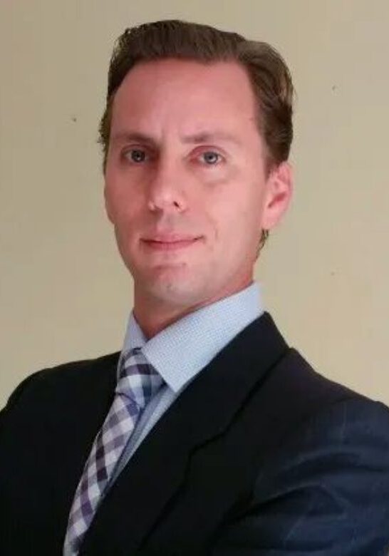 A man in a suit and tie standing up against a wall.